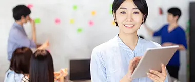 Woman smiling while holding a tablet in a modern office with colleagues in the background