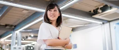 Woman smiling with a notebook in her hands, standing in a bright office space