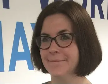 Professional woman with glasses smiling in front of a Hays background wall