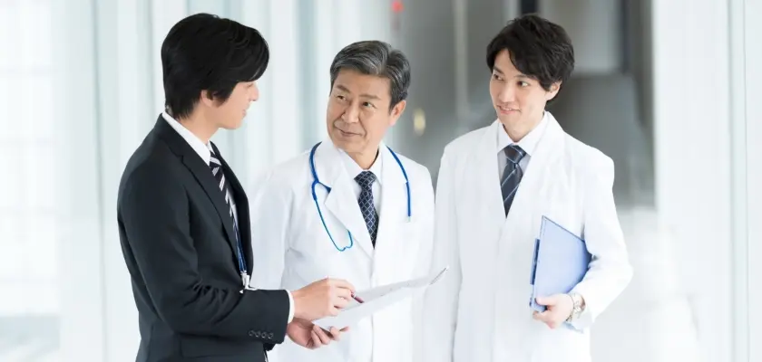 スーツ姿の男性と白衣を着た医師たちが会話する場面