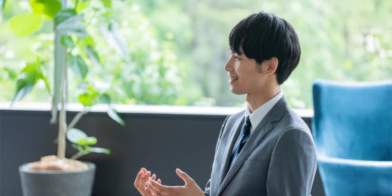 明るいオフィスで前向きに話すグレースーツの男性。