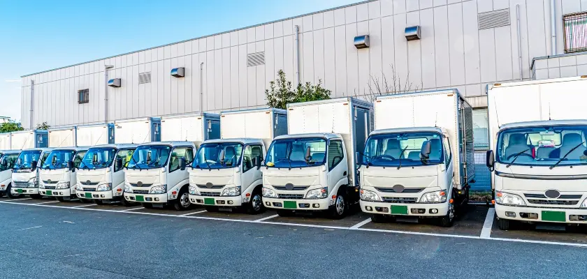日本の物流倉庫の外に停車している白い配送トラックの列